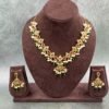 Traditional gold necklace featuring intricate floral motifs with green and maroon colored stones and white pearl drops
