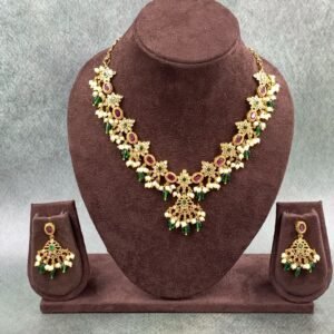 Traditional gold necklace featuring intricate floral motifs with green and maroon colored stones and white pearl drops