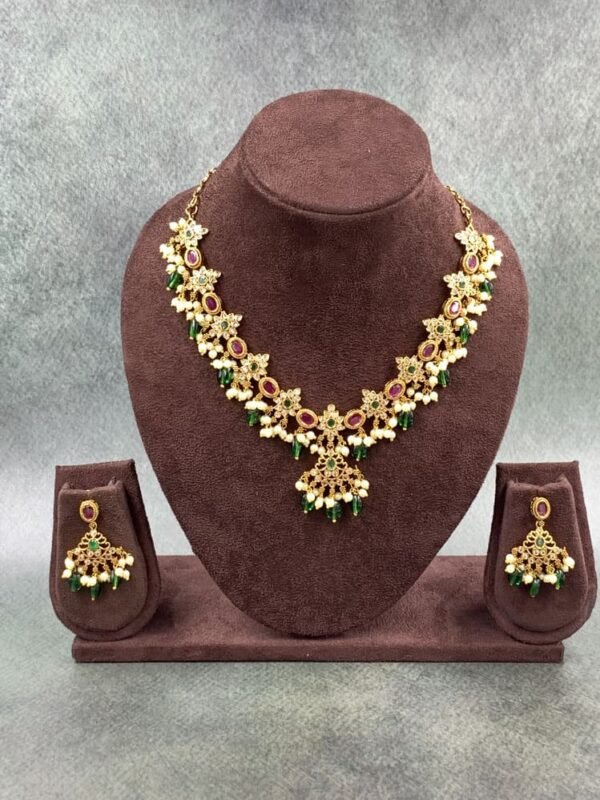 Traditional gold necklace featuring intricate floral motifs with green and maroon colored stones and white pearl drops