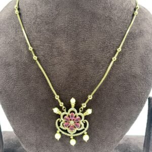 Elegant gold necklace featuring floral pendant with pink stones and pearl drops displayed on gray jewelry stand