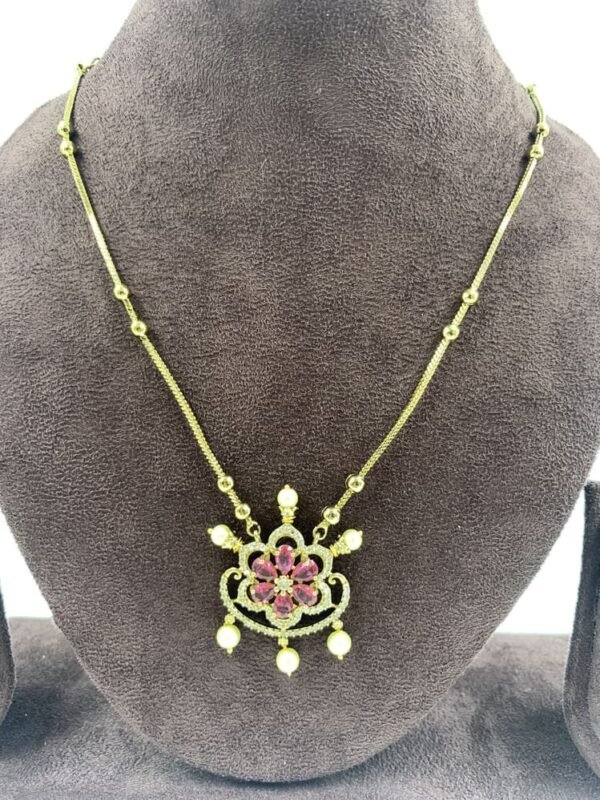 Elegant gold necklace featuring floral pendant with pink stones and pearl drops displayed on gray jewelry stand